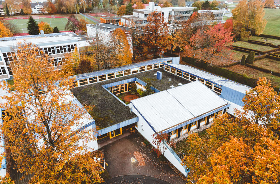 Schulgebäude von oben, mit Blick auf Sportplatz und Hallenbad